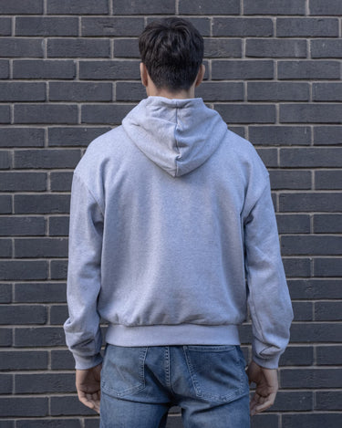 Model wearing a heather Grimboy hoodie and jeans standing against a brick wall.